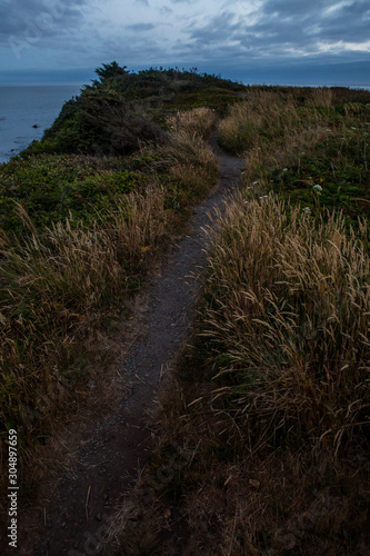 Sunset hike on the coast. Coast trail overlooking ocean. Hiking through sunset meadow.