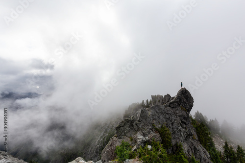 Adventurous Man Standing on top of a rugged rocky mountain during a cloudy summer morning. Taken on Crown Mountain, North Vancouver, BC, Canada. © edb3_16