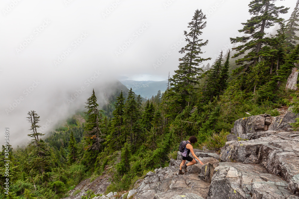 Adventurous Girl is hiking in beautiful green woods in the mountains during a cloudy summer morning. Taken on Crown Mountain, North Vancouver, BC, Canada.
