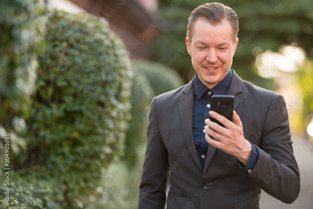 Happy young handsome businessman in suit using phone outdoors Happy young handsome businessman in suit using phone outdoors