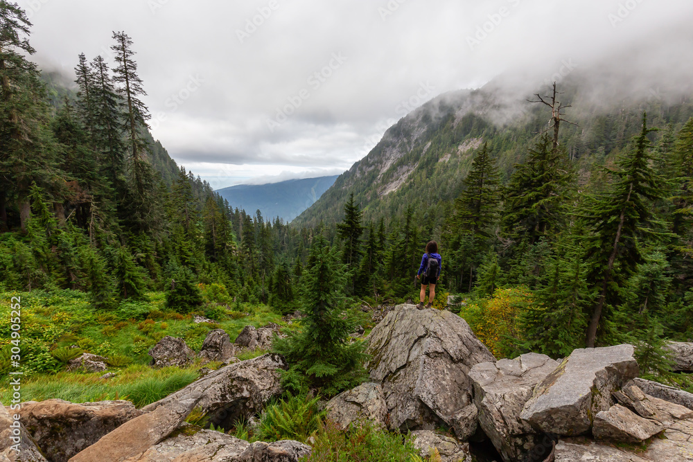Adventurous Girl is hiking in beautiful green woods in the mountains during a cloudy summer morning. Taken on Crown Mountain, North Vancouver, BC, Canada. Adventurous Girl is hiking in beautiful green woods in the mountains during a cloudy summer morning. Taken on Crown Mountain, North Vancouver, BC, Canada.