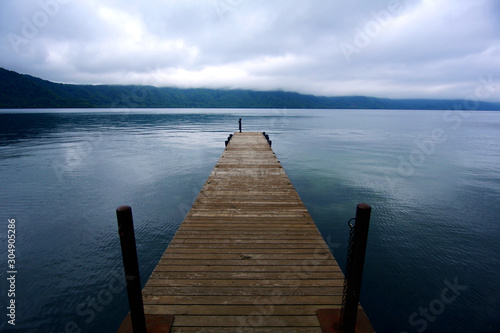 A wooden boardwalk pier extending to the lake  adding more stories to the tranquil lake. Imagine it is very beautiful