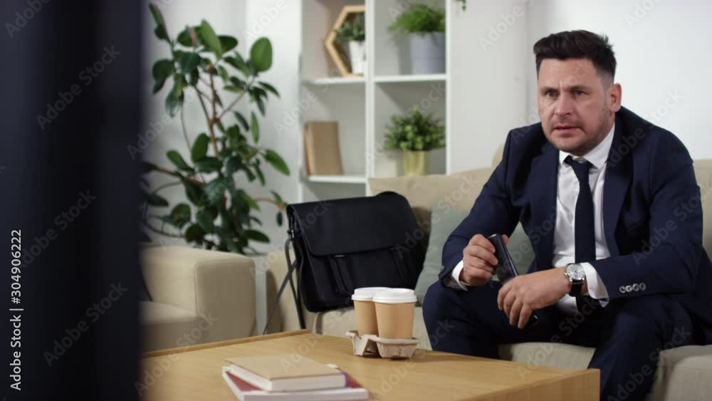 Anxious middle aged businessman in formalwear sitting on couch at home and watching sport match on TV. He yelling in excitement, clapping hands and kissing remote control as his favorite team winning Anxious middle aged businessman in formalwear sitting on couch at home and watching sport match on TV. He yelling in excitement, clapping hands and kissing remote control as his favorite team winning