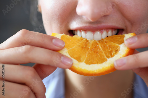 Beautiful brunette smiling woman eat sliced orange