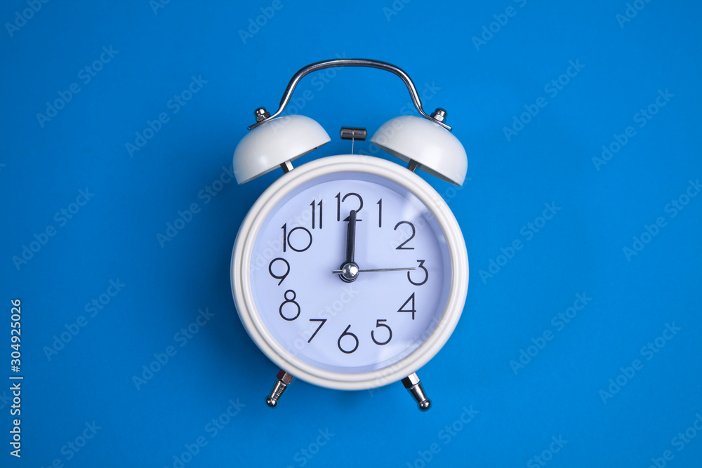 A white alarm clock on a blue background. a top view. a close-up picture representing 12 o'clock A white alarm clock on a blue background. a top view. a close-up picture representing 12 o'clock