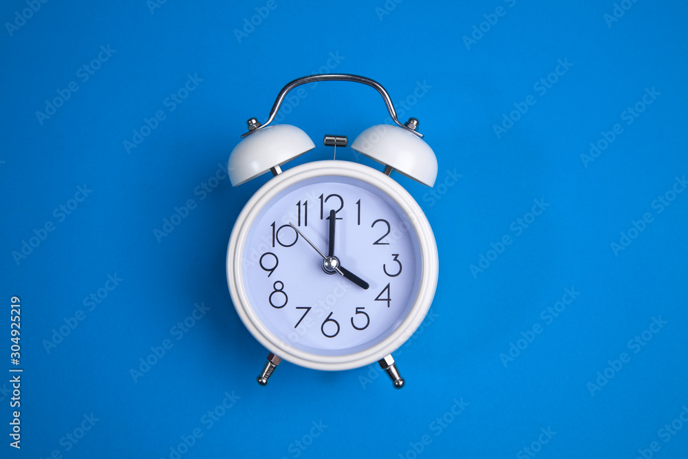 A white alarm clock on a blue background. a top view. a close-up picture representing 4 o'clock A white alarm clock on a blue background. a top view. a close-up picture representing 4 o'clock