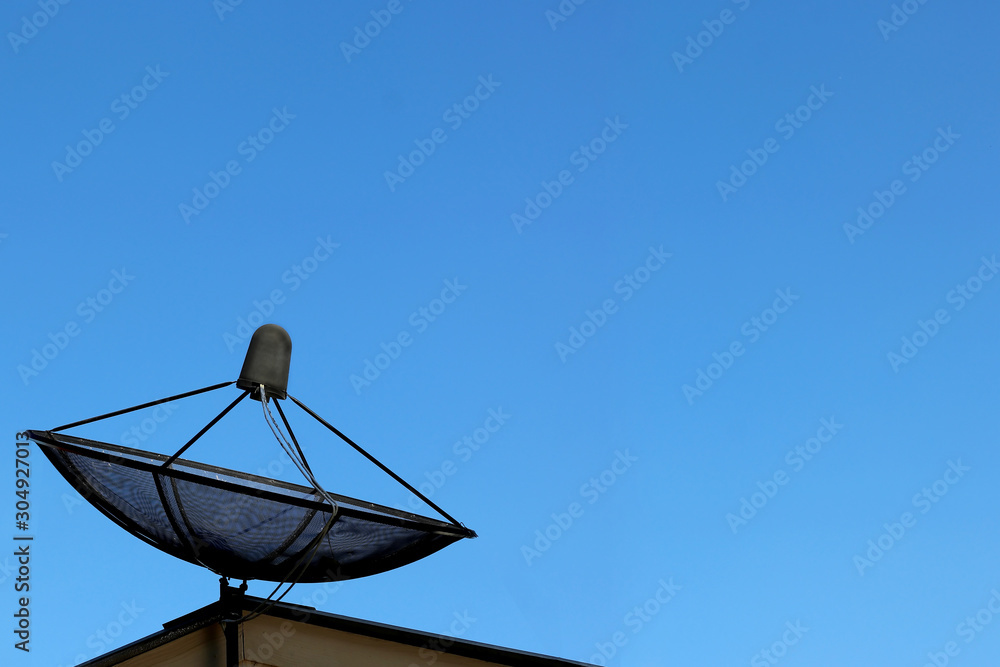 Black network satellite disc on roof on blue sky background