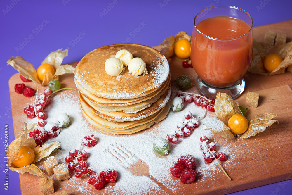 A stack of pancakes with icing sugar and a glass of juice on the table. A stack of pancakes with icing sugar and a glass of juice on the table.