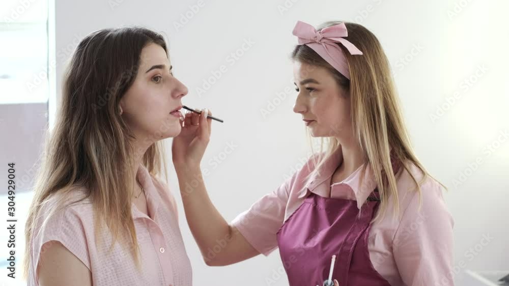 The girls wear pink clothes. Makeup artist puts lipstick. The girl makes a makeup. The girls wear pink clothes. Makeup artist puts lipstick. The girl makes a makeup.