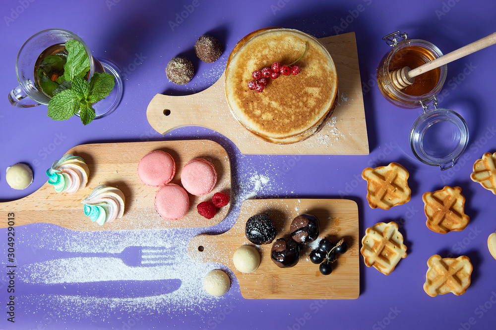Pancakes with honey and sweets on a purple background, top view. Pancakes with honey and sweets on a purple background, top view.