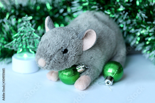 Cute rat or mouse soft toy with green ornaments and tinsel. Chinese New Year symbol. Festive background with copy space for text. Poster or greeting card template