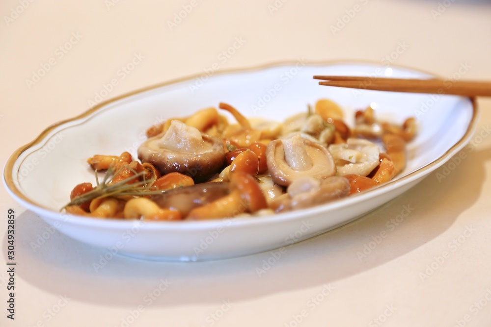 Mushrooms are small salty in sauce wet on a plate of white and sticks for eating Mushrooms are small salty in sauce wet on a plate of white and sticks for eating