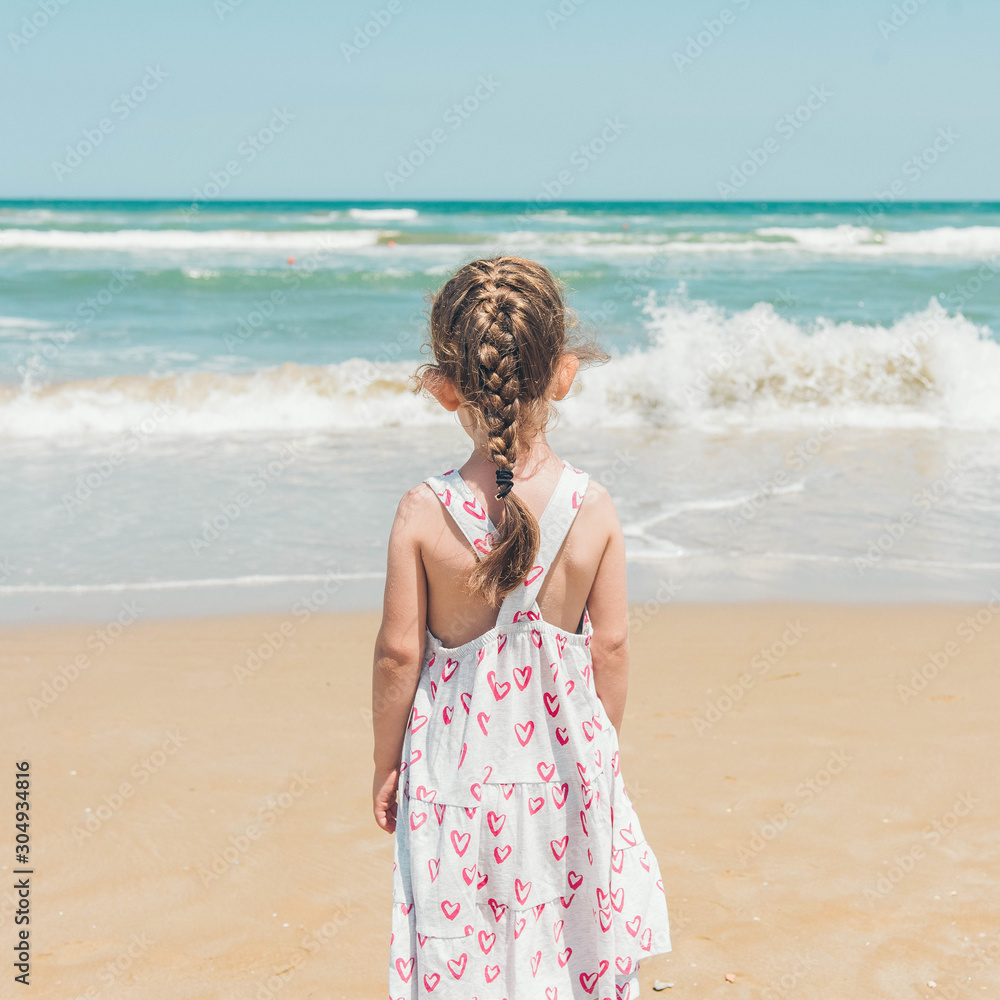 Back view of little girl playing on the sand beach next to the Adriatic sea. Rimini. Italy. Back view of little girl playing on the sand beach next to the Adriatic sea. Rimini. Italy.