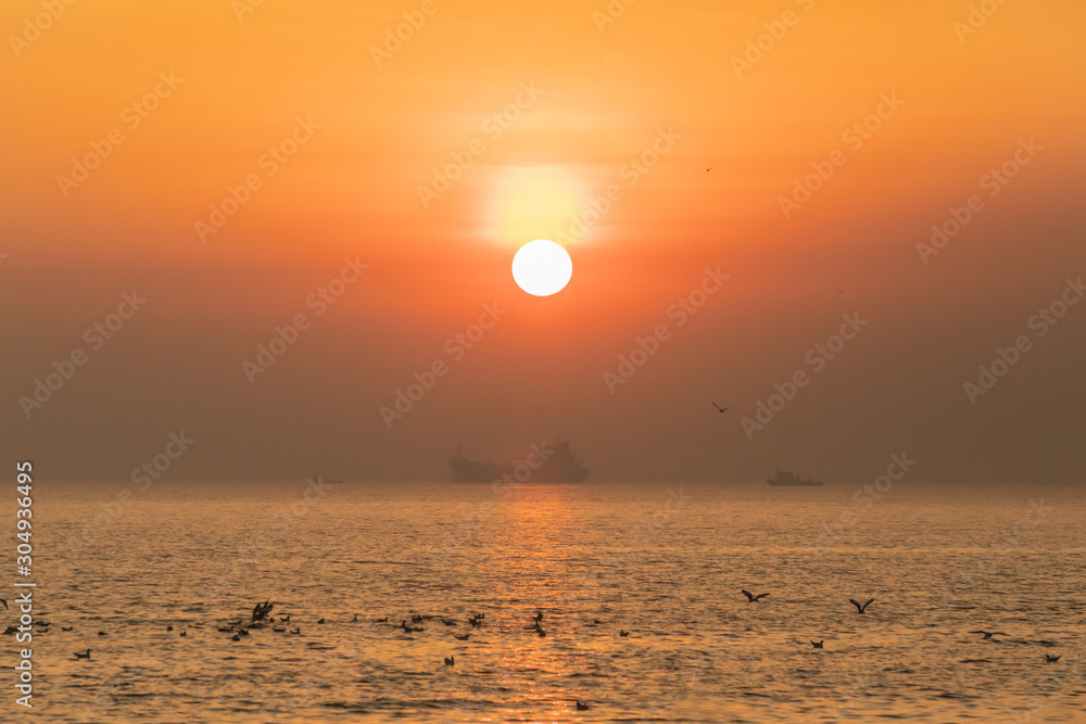 Sunset or evening time with golden sky at sea or ocean with cargo ship and seagull bird flying at Bang poo, Samutprakan, Thailand.