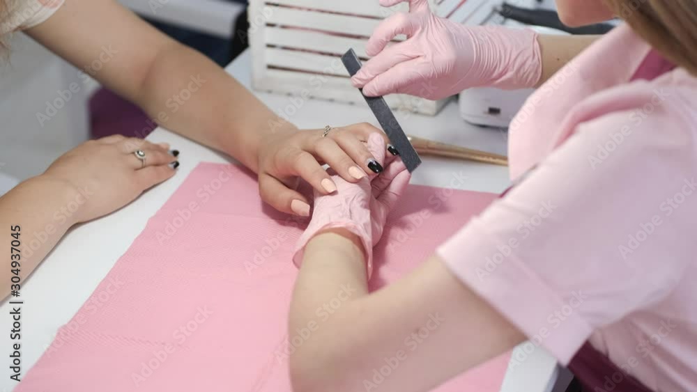 A manicurist wears the pink gloves. A table is white. The girl uses the manicure tools. A manicurist wears the pink gloves. A table is white. The girl uses the manicure tools.