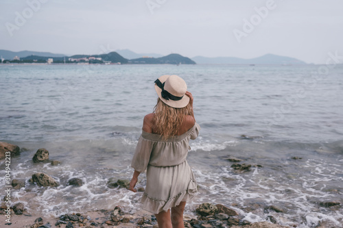 Relaxed woman enjoying ocean bay, freedom and life at beautiful beach coastline in windy cloudy weather. Young lady feeling free, relaxed and happy. Concept of vacations, freedom, happiness, enjoyment