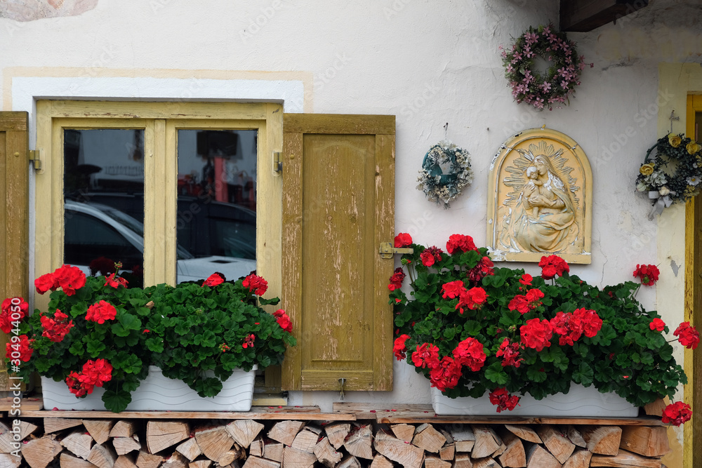 window with shutters, geranium, firewood and christmas wreath
