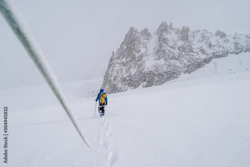 An alpinist walking on a glacier using rope. Detail shot of a climber with a rope in extreme mountain conditions. Adventure ascent of an alpine peak. An alpinist walking on a glacier using rope. Detail shot of a climber with a rope in extreme mountain conditions. Adventure ascent of an alpine peak.