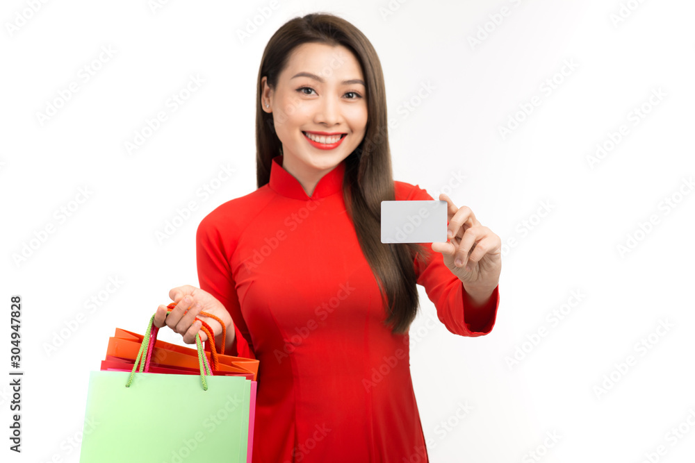 Beautiful Asian young woman in aodai with shopping bags holding credit card over white background Beautiful Asian young woman in aodai with shopping bags holding credit card over white background