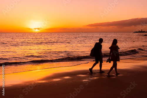 A man and a woman walk along the seashore against the backdrop of the setting sun. Orange sunset at the sea. Silhouettes on a sunset background