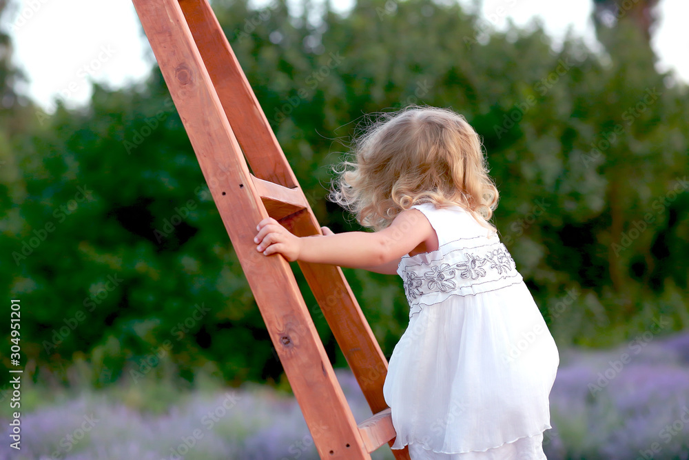 cute little girl in a white dress climbs a wooden staircase in nature cute little girl in a white dress climbs a wooden staircase in nature