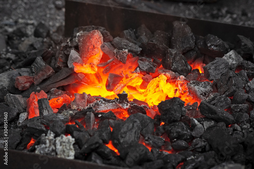 Embers glow in a iron forge in the darkness. Fire, heat, coal and ash.