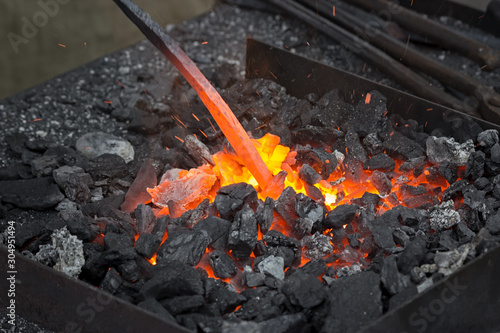 Bar heating for vaking a horseshoe. Embers glow in a iron forge. Fire, heat, coal, ash and blacksmith tools.