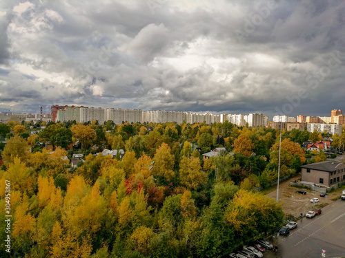Low gray-white Cumulus clouds over yellow-green trees and tall houses on the horizon
