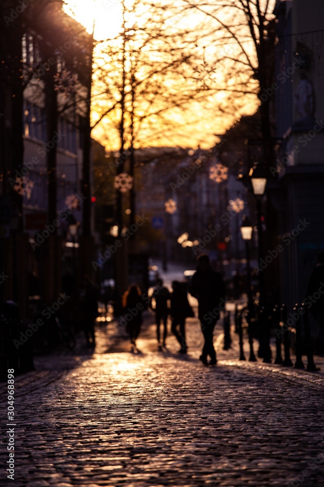 silhouettes of people walking on cobblestone at sunset with christmas decorations