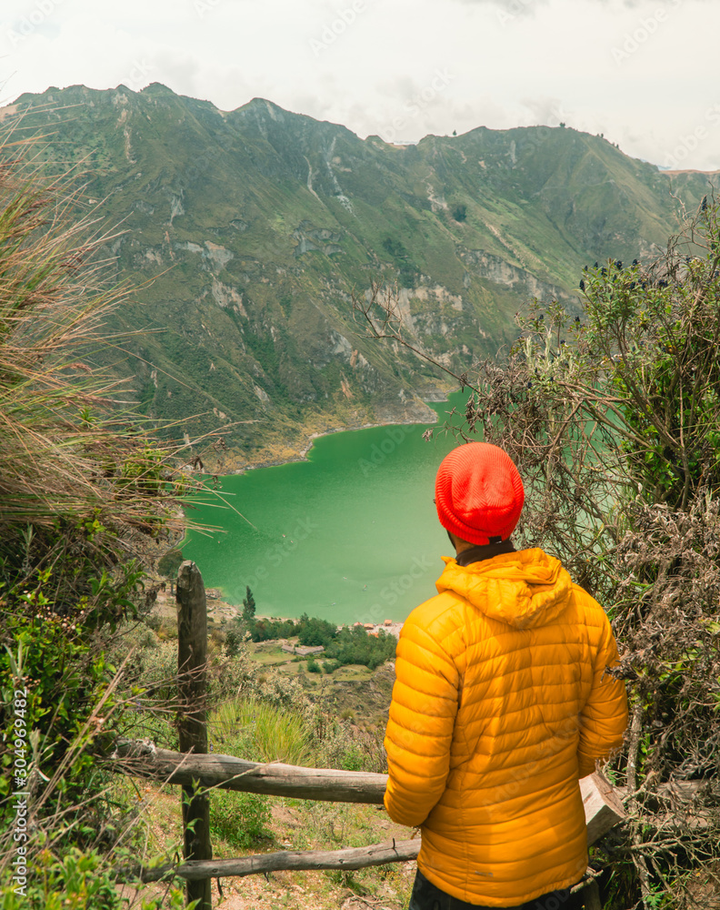 Woman at mountain volcano lake. Hiker in red looking at dramatic perspective of Quilotoa lake and crater view. Hiking loop from viewpoint. Shot in Ecuador. Green and blue. Freedom, Adventure