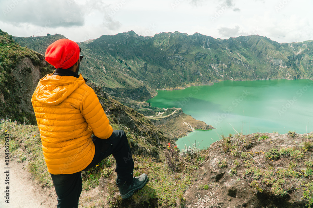 Woman at mountain volcano lake. Hiker in red looking at dramatic perspective of Quilotoa lake and crater view. Hiking loop from viewpoint. Shot in Ecuador. Green and blue. Freedom, Adventure