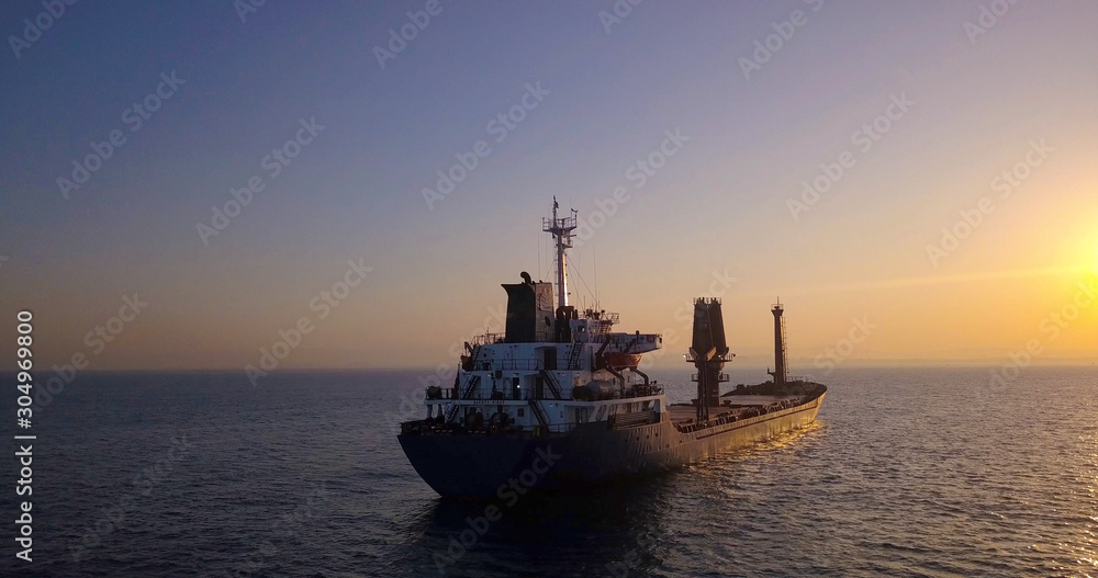 Obraz premium Large Cargo Ship facing Sunrise with flare.