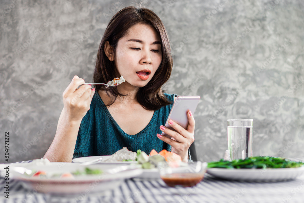 Asian woman using mobile phone while eating dinner at home,internet, social media addiction concept Asian woman using mobile phone while eating dinner at home,internet, social media addiction concept