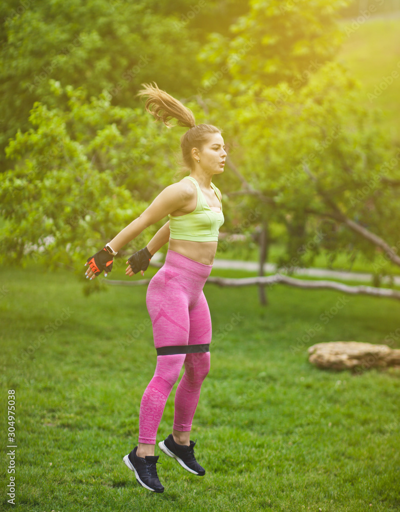 Sporty woman jumping with fitness gum expander in the park outdoors