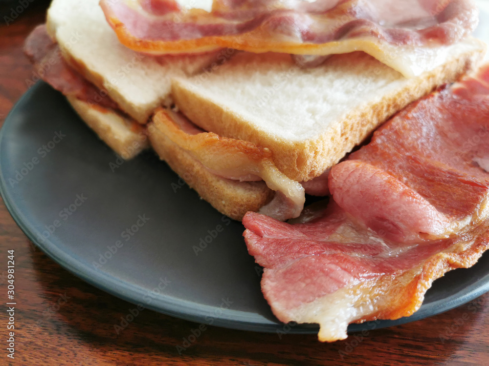 Bacon sandwich on a black plate. Copy space is on the left corner of the photo. Selective focus. 