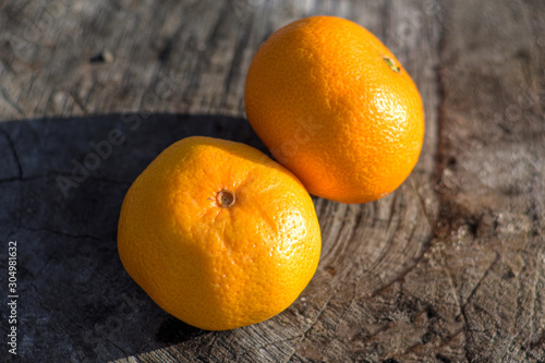 Ripe Mandarin fruit peeled open and place on old rustic look timber with group of mandarin fruits and leaves out of focus on the background