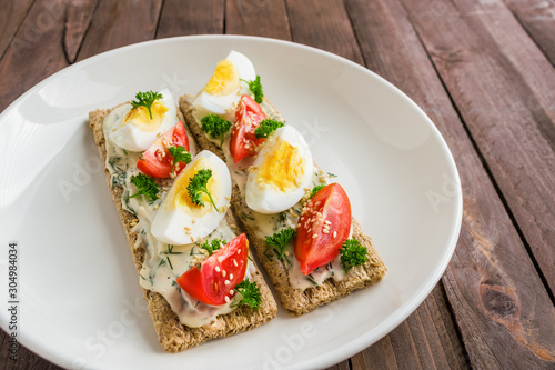 open crispbread sandwiches with boiled eggs fresh tomatoes cream cheese on white plate . healthy food