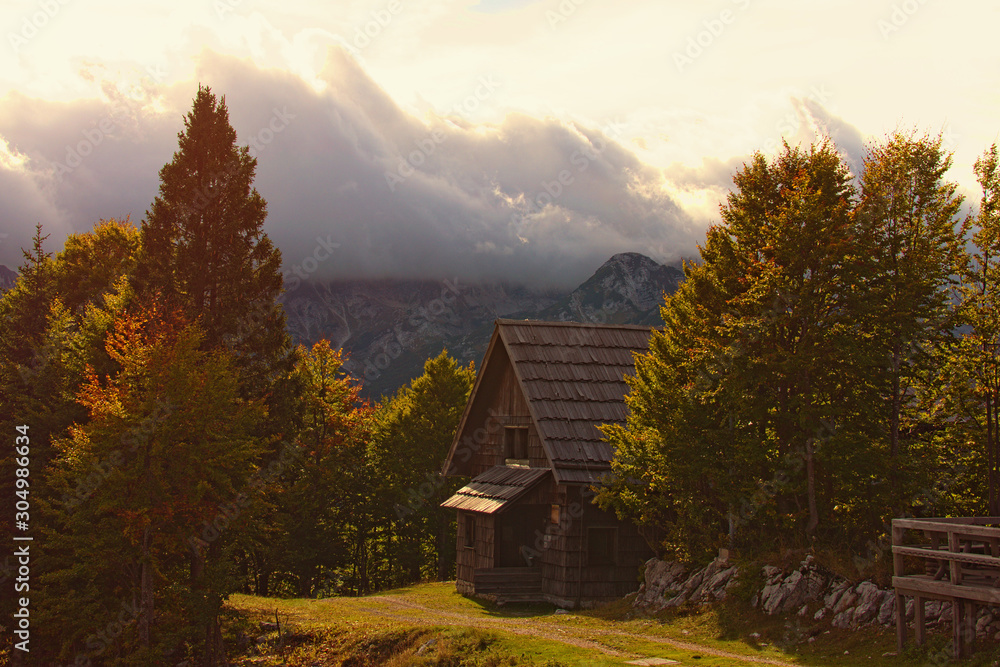 Magic mountain autumn landscape. Wooden shelter in the autumn color forest. High mountain peaks with thunderclouds. Dramatic scene. Concept of landscape and nature. Vogel ski center, Slovenia Magic mountain autumn landscape. Wooden shelter in the autumn color forest. High mountain peaks with thunderclouds. Dramatic scene. Concept of landscape and nature. Vogel ski center, Slovenia