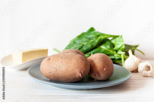  organic potatoes on a gray plate on a white table  with ingredients for mashed potatoes. spinach  butter and garlic