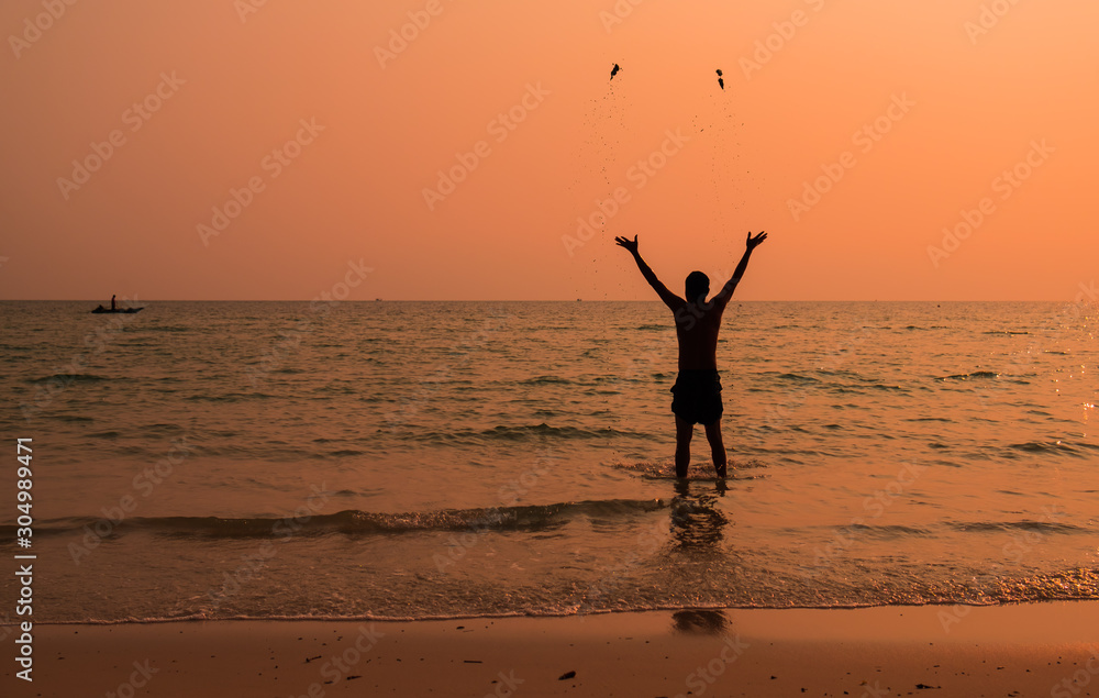 Silhouette photograph of the man is standing back in the sea and throw away the sand with fully happy moment with beautiful sunset light. 