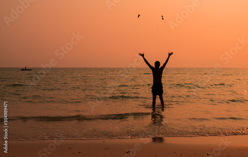 Silhouette photograph of the man is standing back in the sea and throw away the sand with fully happy moment with beautiful sunset light. 