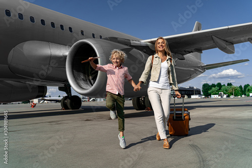 Happy woman walking with suitcase near plane