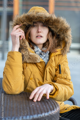 Young blond caucasian woman posing winter outdoor. Beautiful girl, urban portrait. Fashion model sitting and looking at camera