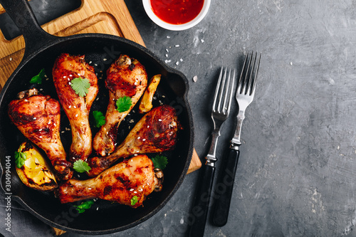 Roasted Lemon Chicken Legs with chili sauce and sesame in cast iron pan on dark stone background