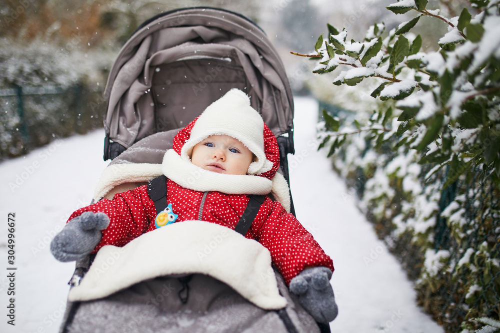 Happy smiling baby girl in stroller in Paris day with heavy snow