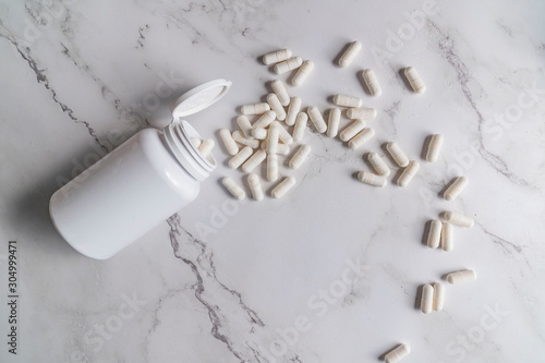 painkillers and drug abuse concept with close up on a bottle of prescription drugs and pill capsules falling out of it on a white marble table