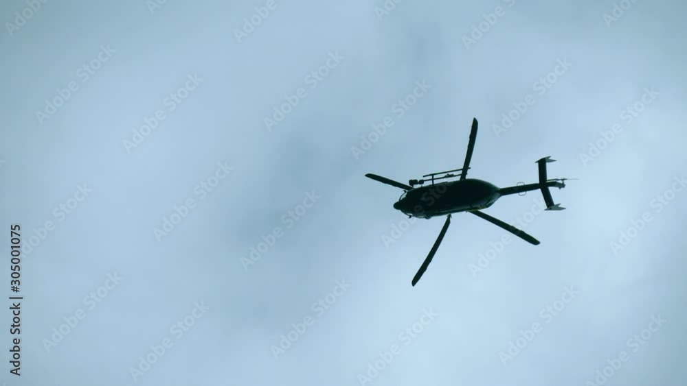 A modern, black helicopter hovers in the sky, as viewed from the bottom up. Silhouette of a modern helicopter hovering in the sky, the blades spin slowly. A modern, black helicopter hovers in the sky, as viewed from the bottom up. Silhouette of a modern helicopter hovering in the sky, the blades spin slowly.