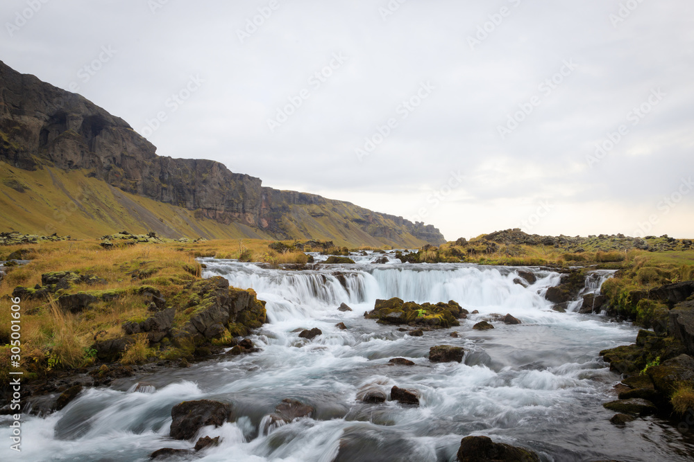 Panoramic summer view of small waterfall near Bjodvegur road. Wonderful sunrise on Iceland, Vik location. Beauty of nature concept background..
