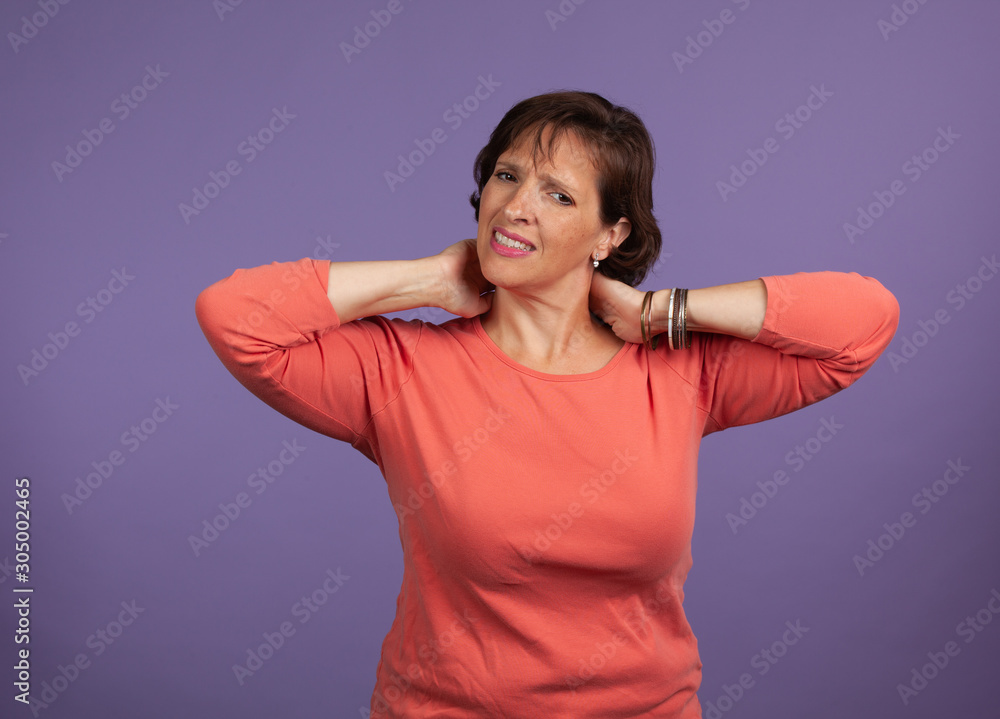 Fototapeta premium Middle Aged woman with neck and shoulder pain holding her neck and making a pained expression.