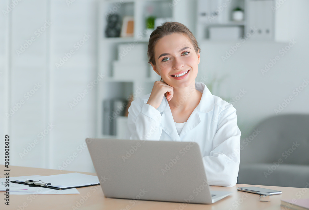 Female doctor with laptop sitting at table in clinic - obrazy, fototapety, plakaty 